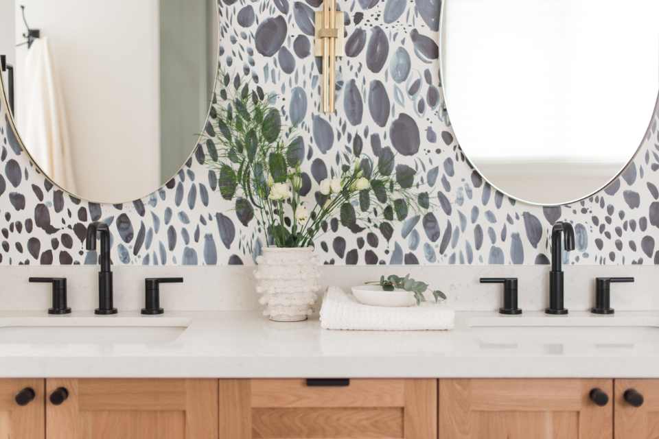 blue stone-look wallpaper in bathroom with gold accents, wood cabinetry and greenery